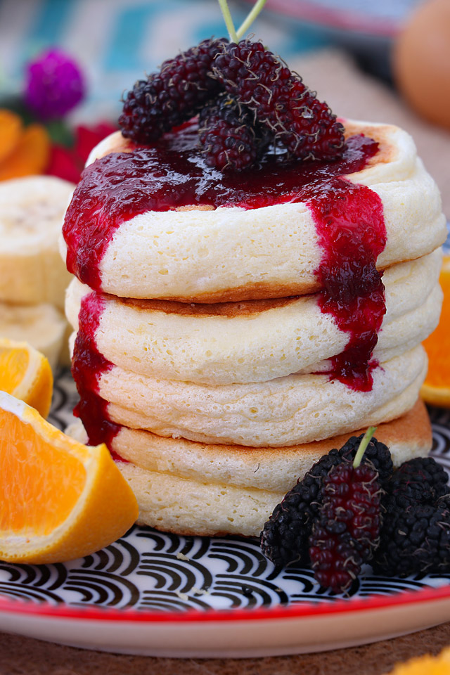 Fluffy souffle pancakes with jam on top and fruits.