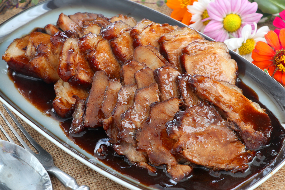 Thin slices of pork with dark, sweet, sticky sauce serve on a plate.