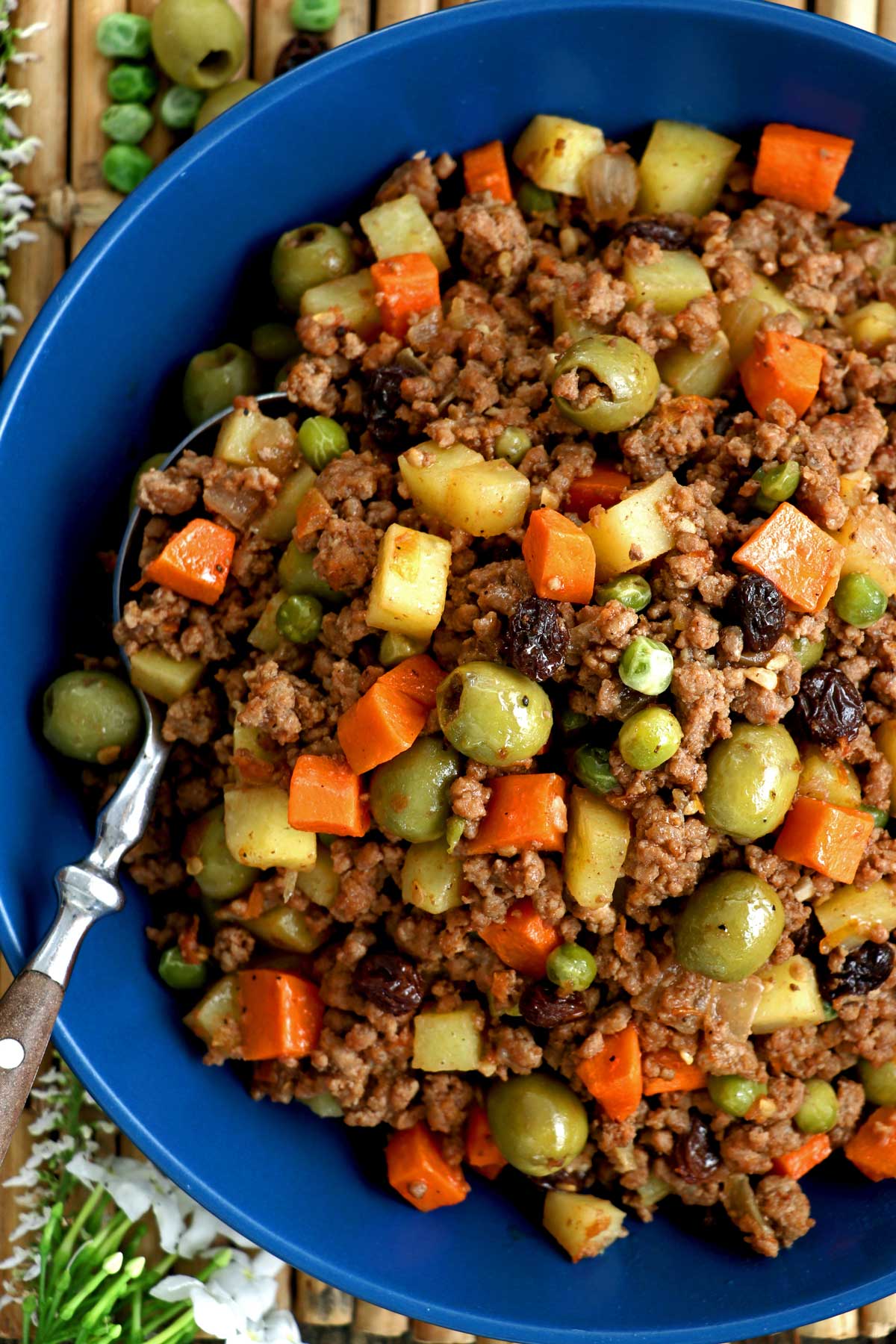 Picadillo recipe complete with ground beef, potatoes, carrots, olives, green peas, and raisins cooked in fresh tomatoes.