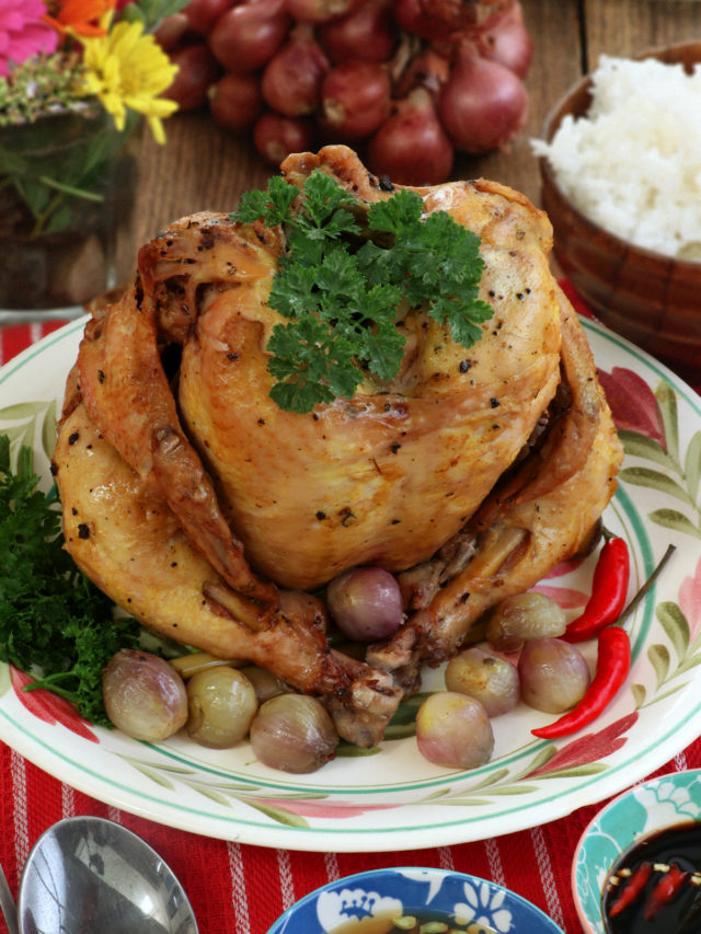 Whole chicken cooked upright on a bed of rock salt in a pot.