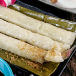 Suman Malagkit on unwrapped banana leaf served with a choice of sugar and latik sauce.