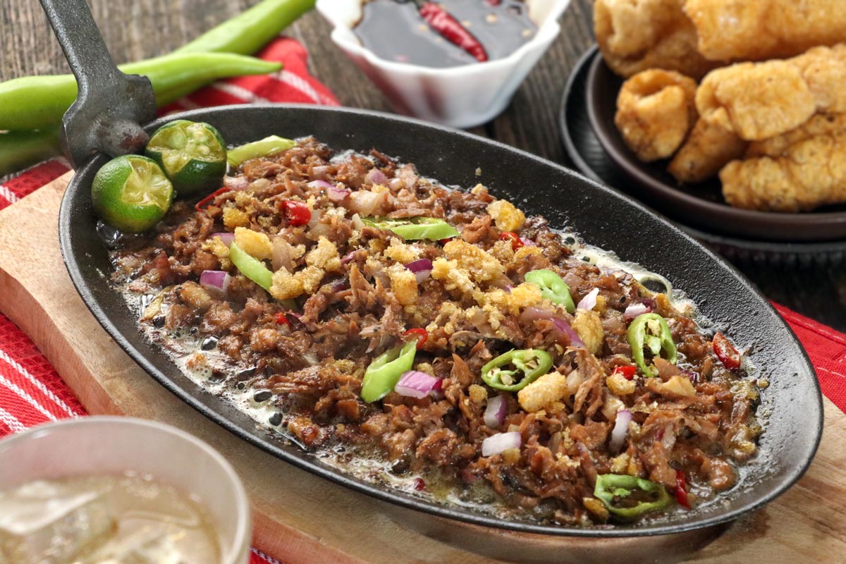 Tuna Sisig on a sizzling plate garnished with chicharon and chilis and served with spiced soy sauce.