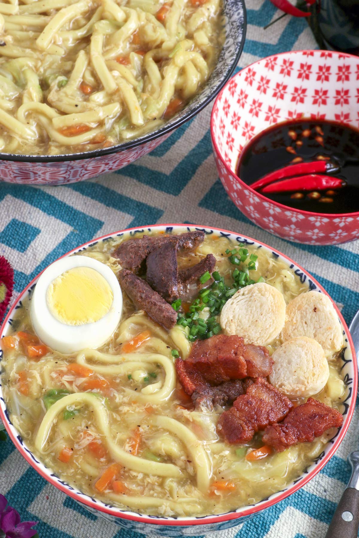 Pancit Lomi in a bowl with a thick rich broth and egg noddles topped with squid balls, pork liver, hard boiled eggs and pork cracklings.