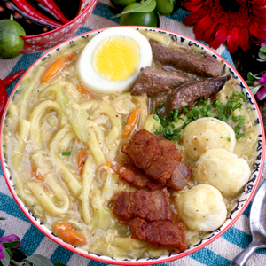 Pancit Lomi in a bowl with a thick rich broth and egg noddles topped with squid balls, pork liver, hard boiled eggs and pork cracklings.