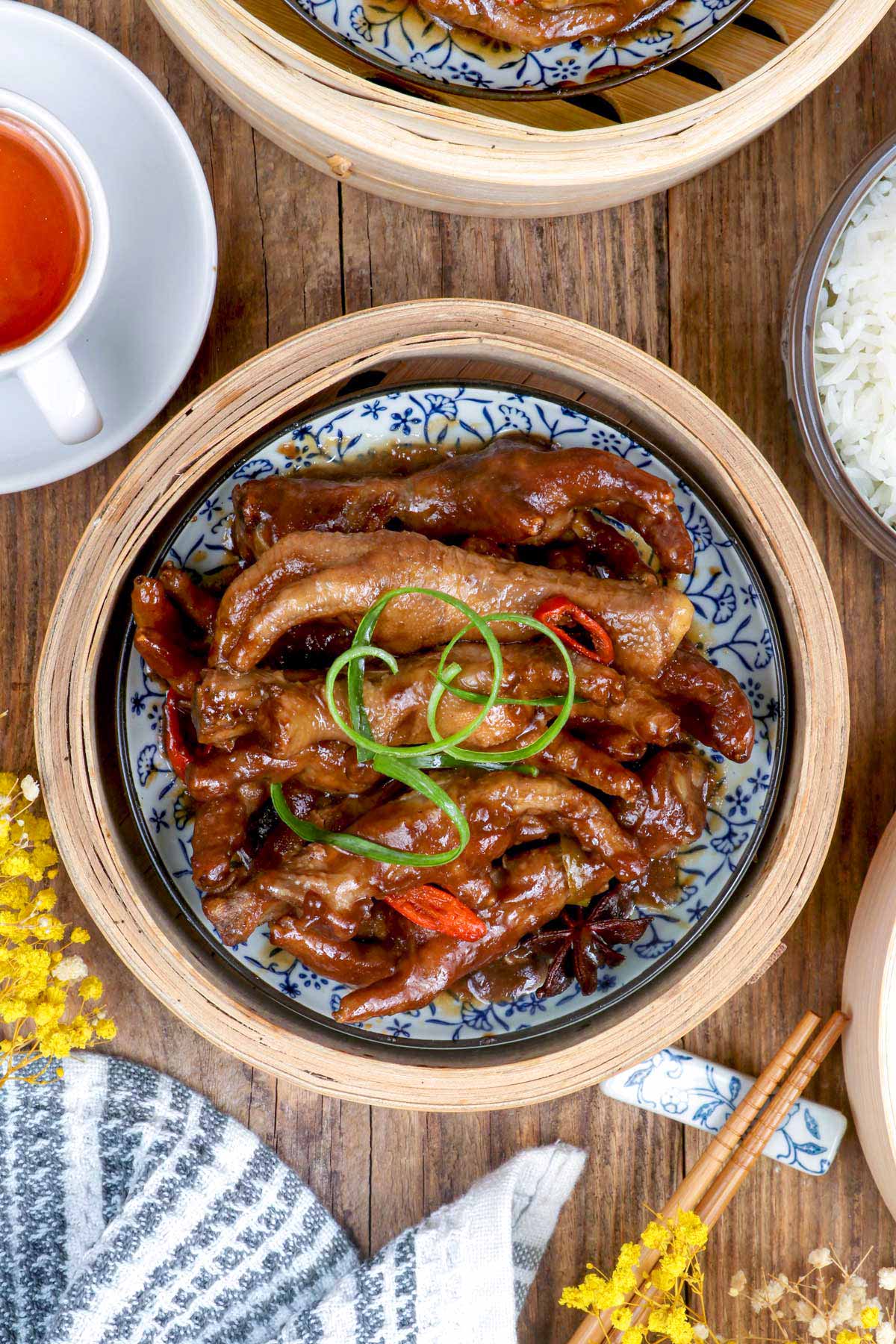 Chicken Feet Dimsum in a bamboo steamer with Thai chilis and star anise. garnished with spring onion.