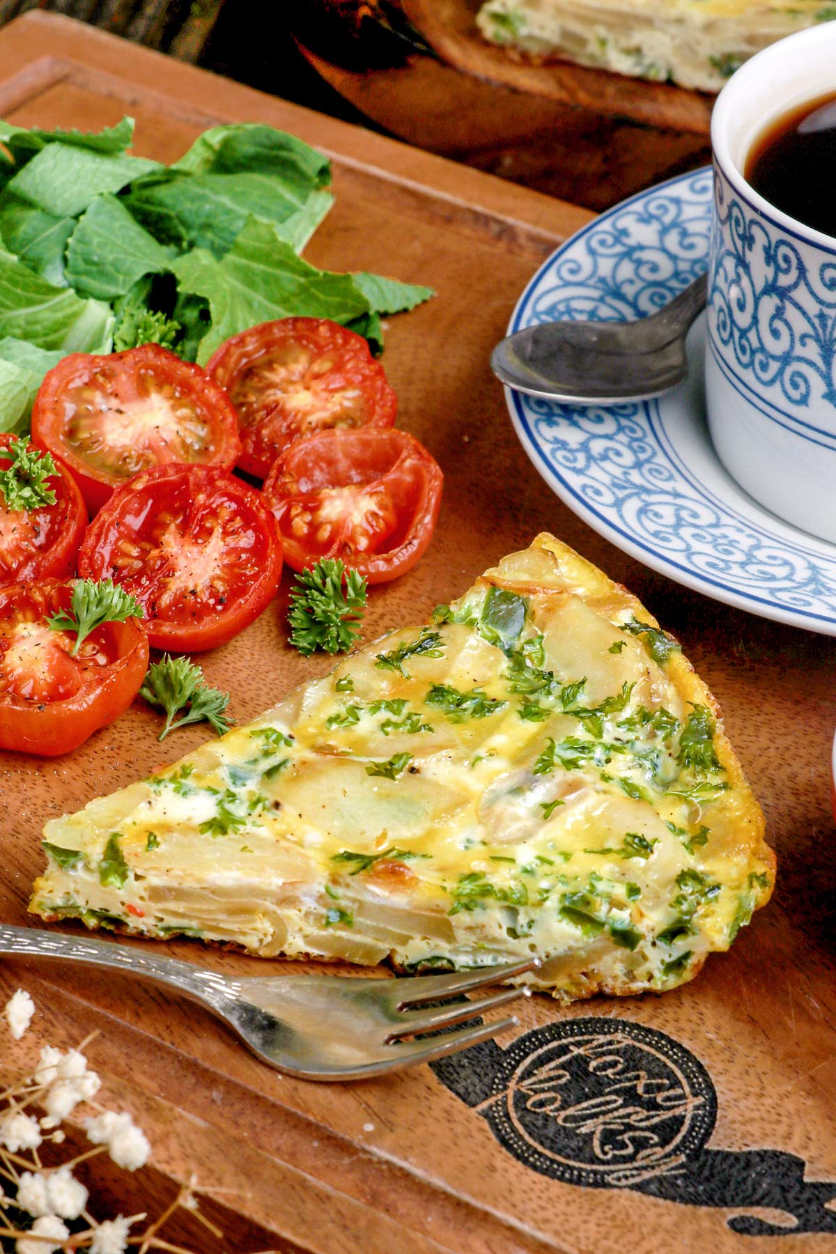Sliced Potato Frittata on a serving board with roasted tomatoes and coffee on the side.
