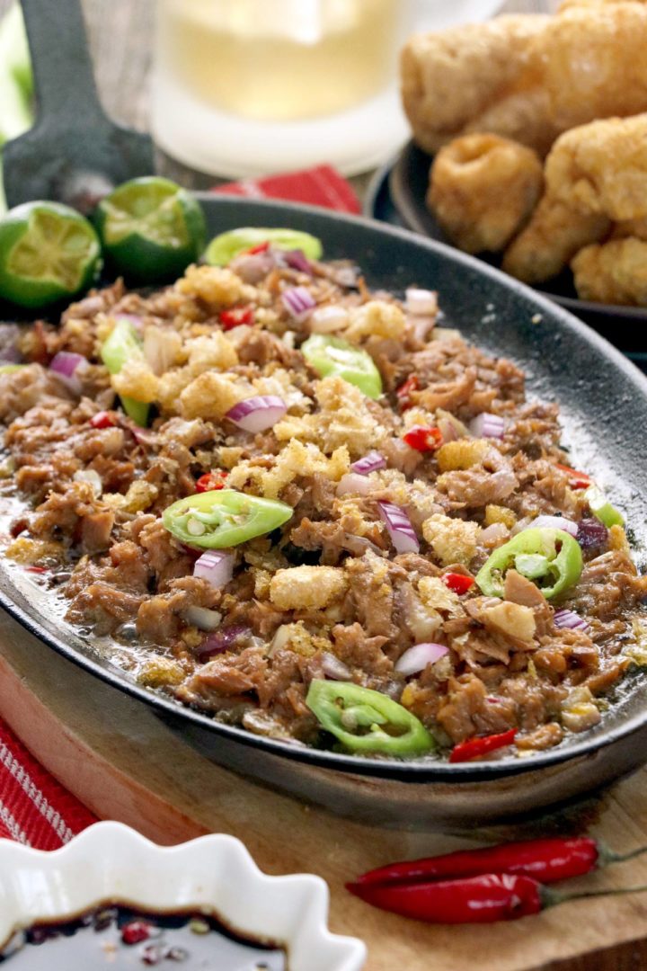 Tuna Sisig on a sizzling plate topped with chicharon and chilis.
