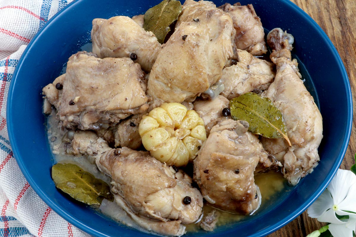 White Adobo in a serving bowl with whole garlic, bay leaves and peppercorns.