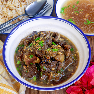 Beef Pares in a serving bowl with fried rice and beef broth on the side.