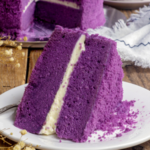 An ube cake slice on a serving plate layered with cream cheese frosting.