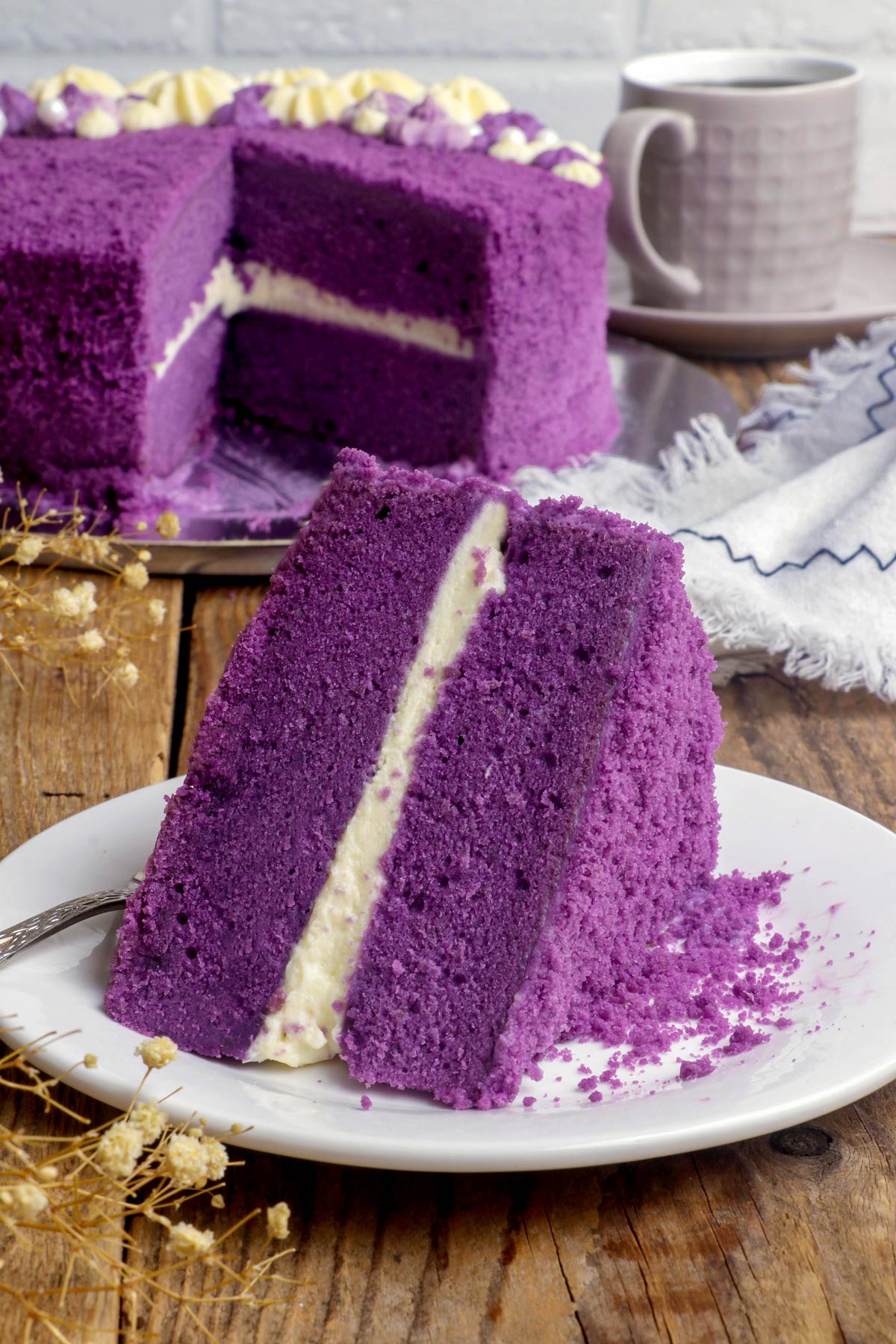 An ube cake slice on a serving plate layered with cream cheese frosting.