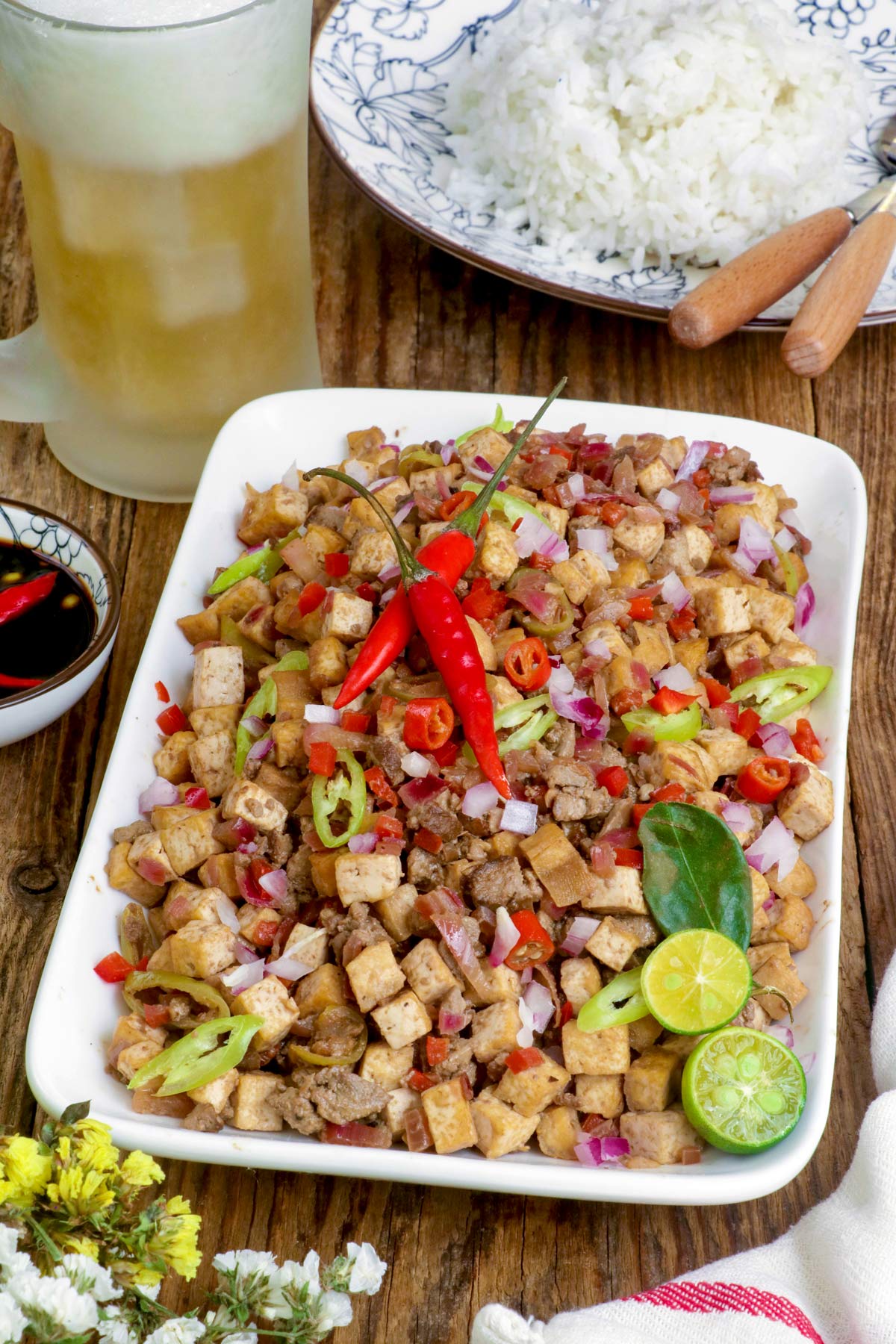 Tofu Sisig on a serving plate with sliced calamansi and red chili served with rice and cold beer.