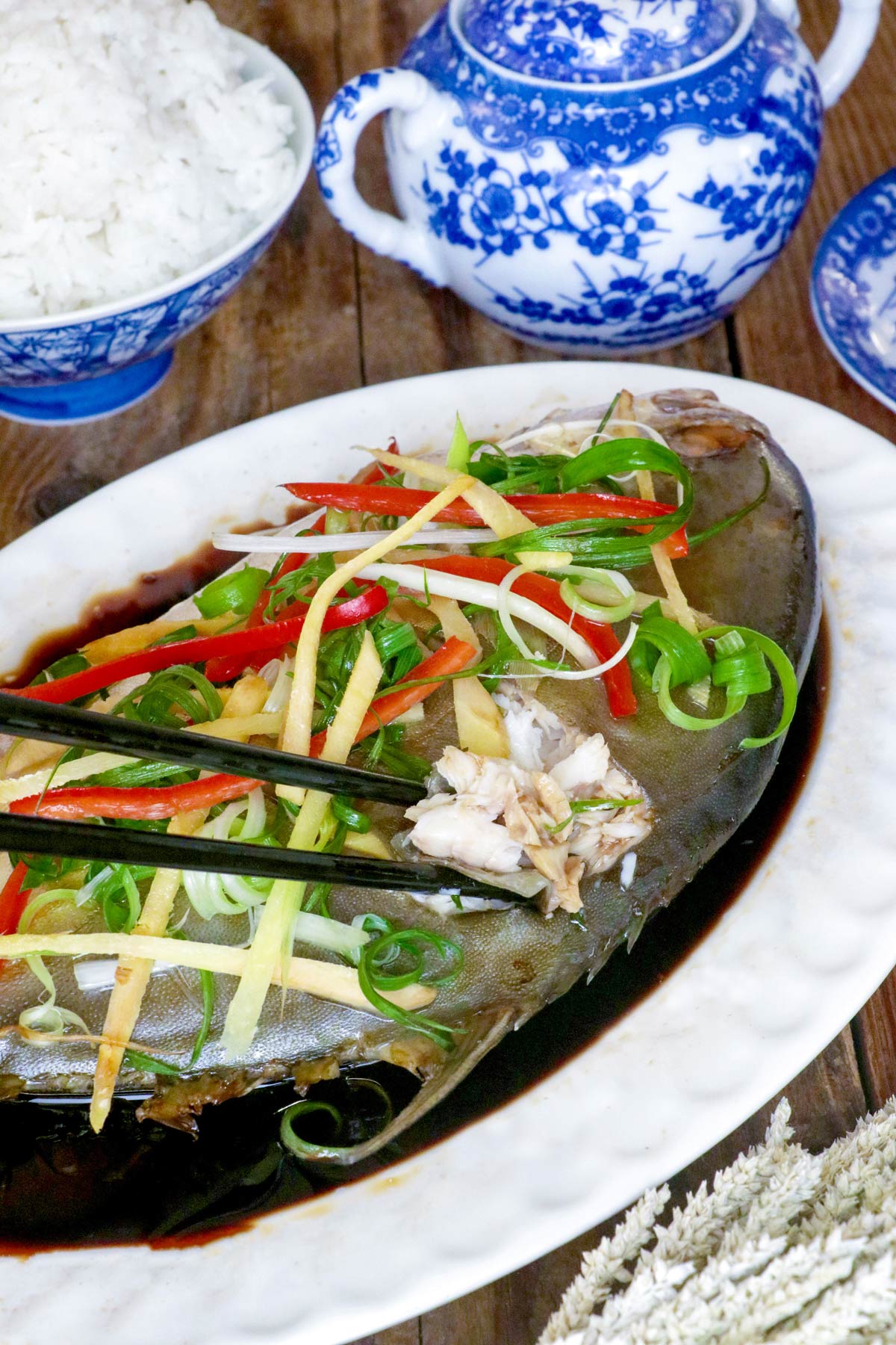 Steamed pompano fish Chinese- style in a serving platter with sliced ginger, green onions, and cilantro on top.