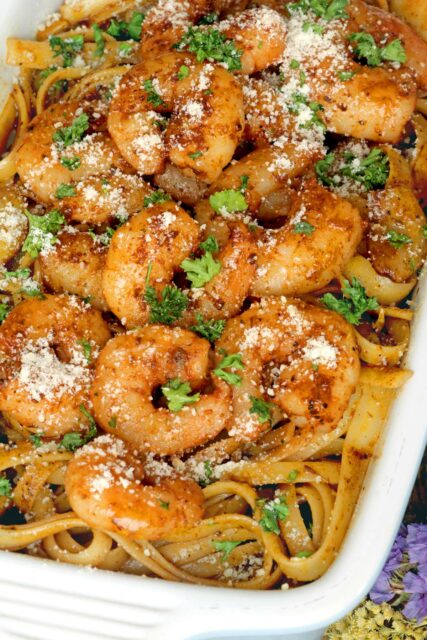 Cajun pasta topped with seared cajun-spiced shrimp, chopped parsley, and parmesan in a serving dish.