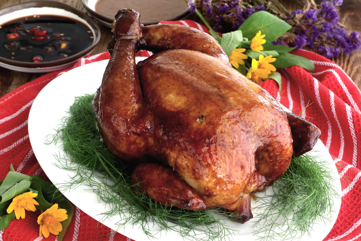 Whole lechon manok on a serving plate with dipping sauces.