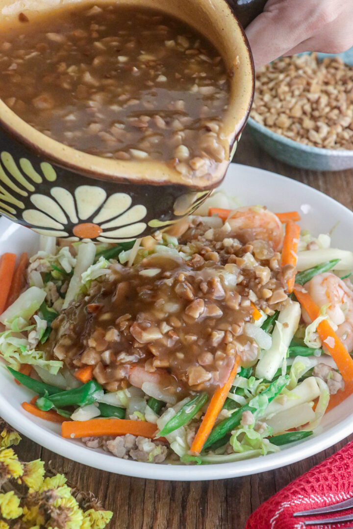 Lumpiang hubad in a serving plate being drizzled with the rich, nutty lumpia sauce.