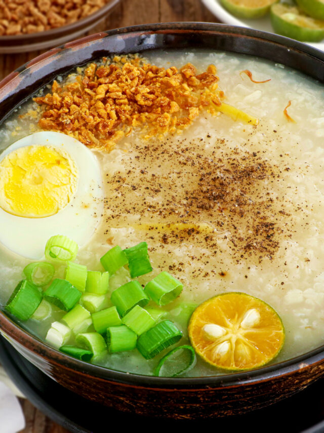 Lugaw in a serving bowl topped with hardboiled egg, fried garlic bits, spring onion, pepper, and calamansi.