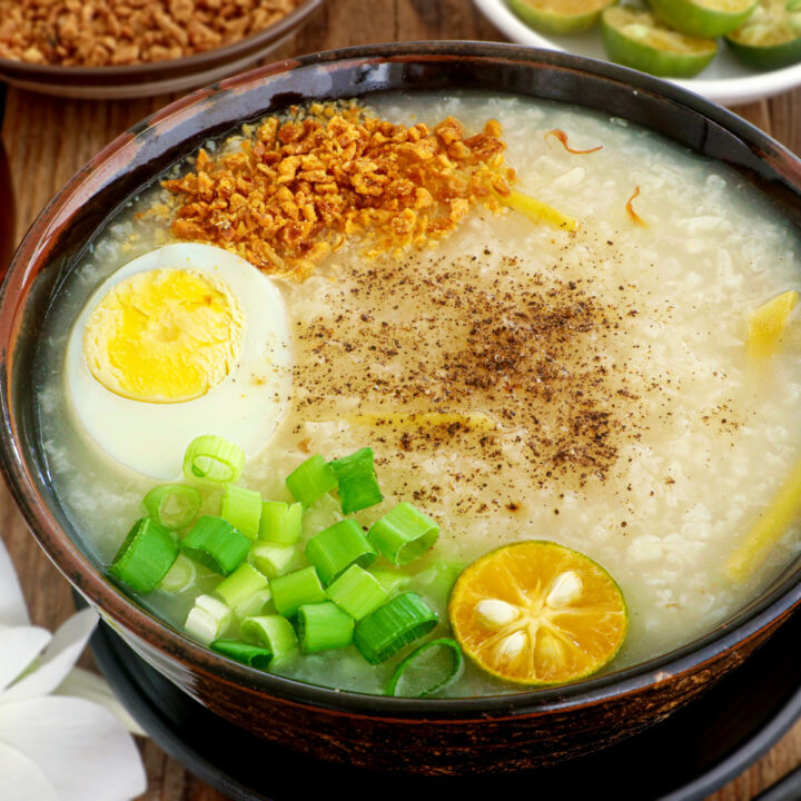 Lugaw in a serving bowl topped with hardboiled egg, fried garlic bits, spring onion, pepper, and calamansi.
