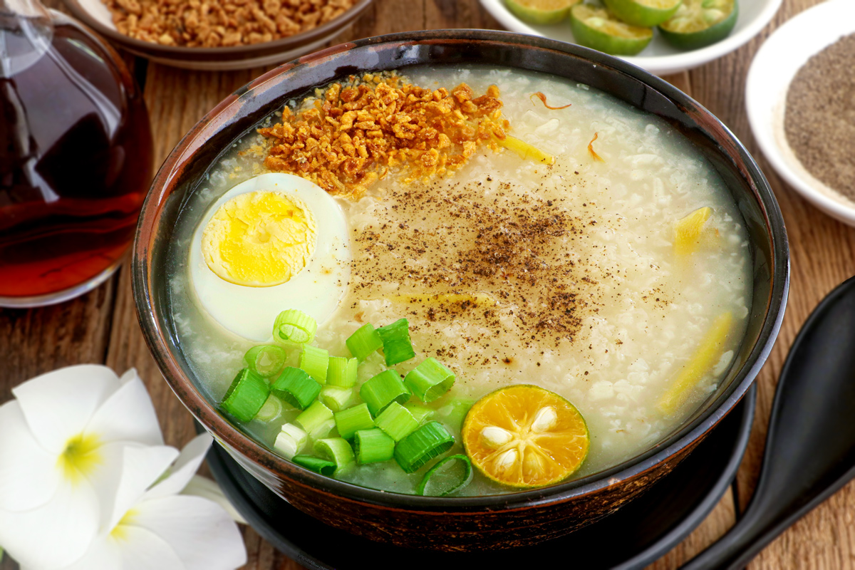 Lugaw in a serving bowl topped with hardboiled egg, fried garlic bits, spring onion, pepper, and calamansi.