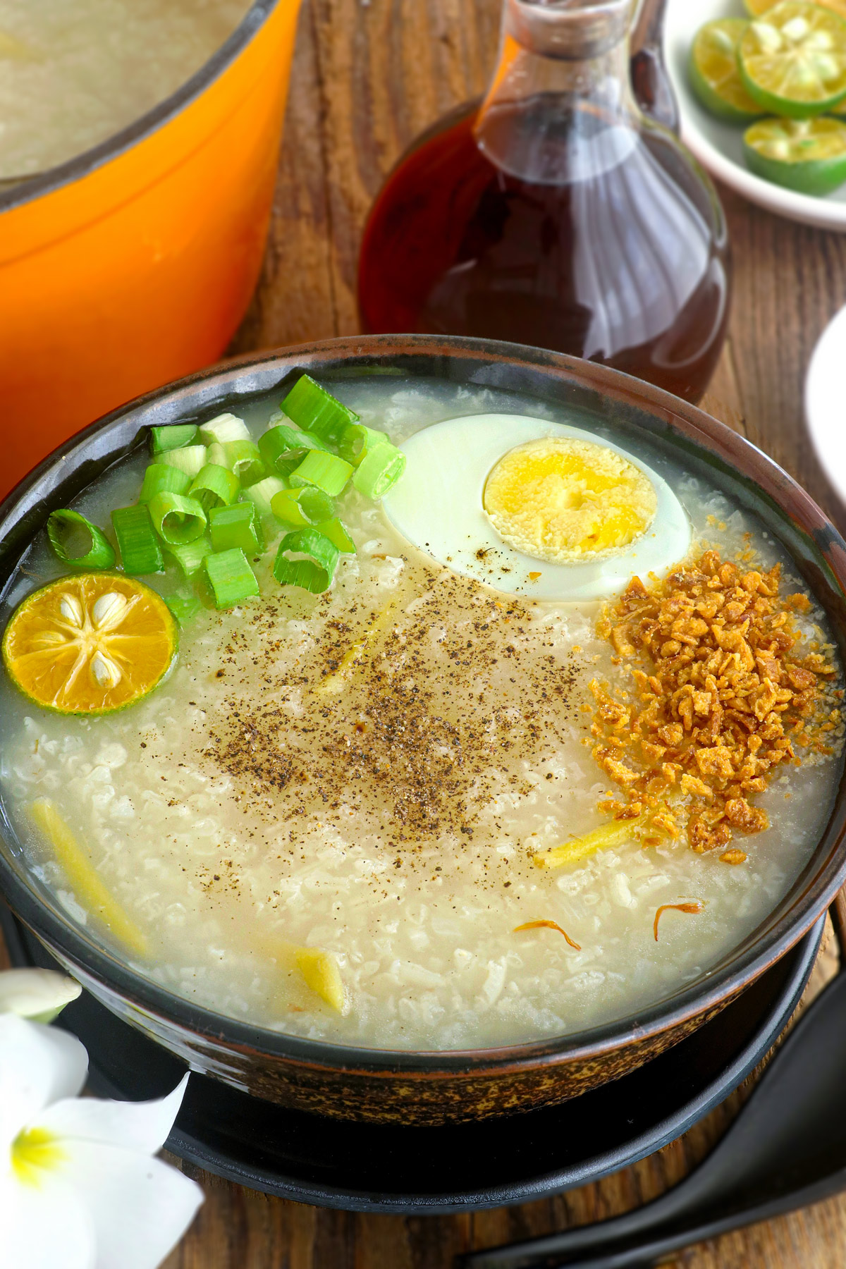 Lugaw in a serving bowl topped with hardboiled egg, fried garlic bits, spring onion, pepper, and calamansi.