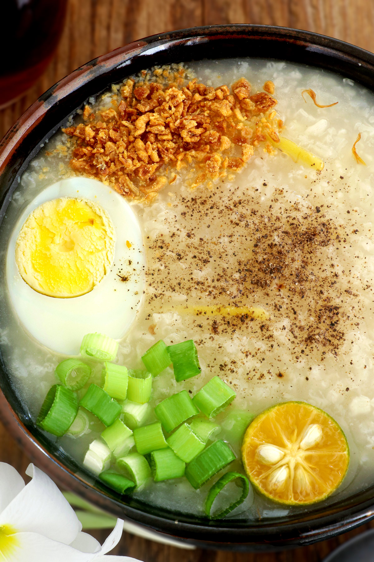 A bowl of hot lugaw with hard-boiled egg, toasted garlic, calamasi, and green onions.